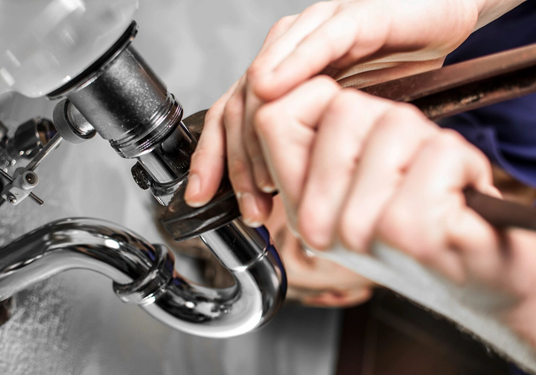 Hands using a wrench to fix a pipe under a sink.