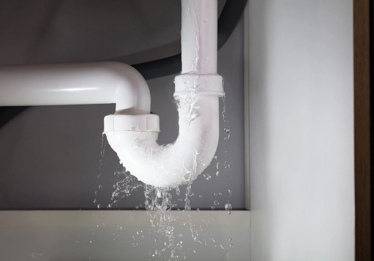 Leaking white pipe under a sink with water dripping.