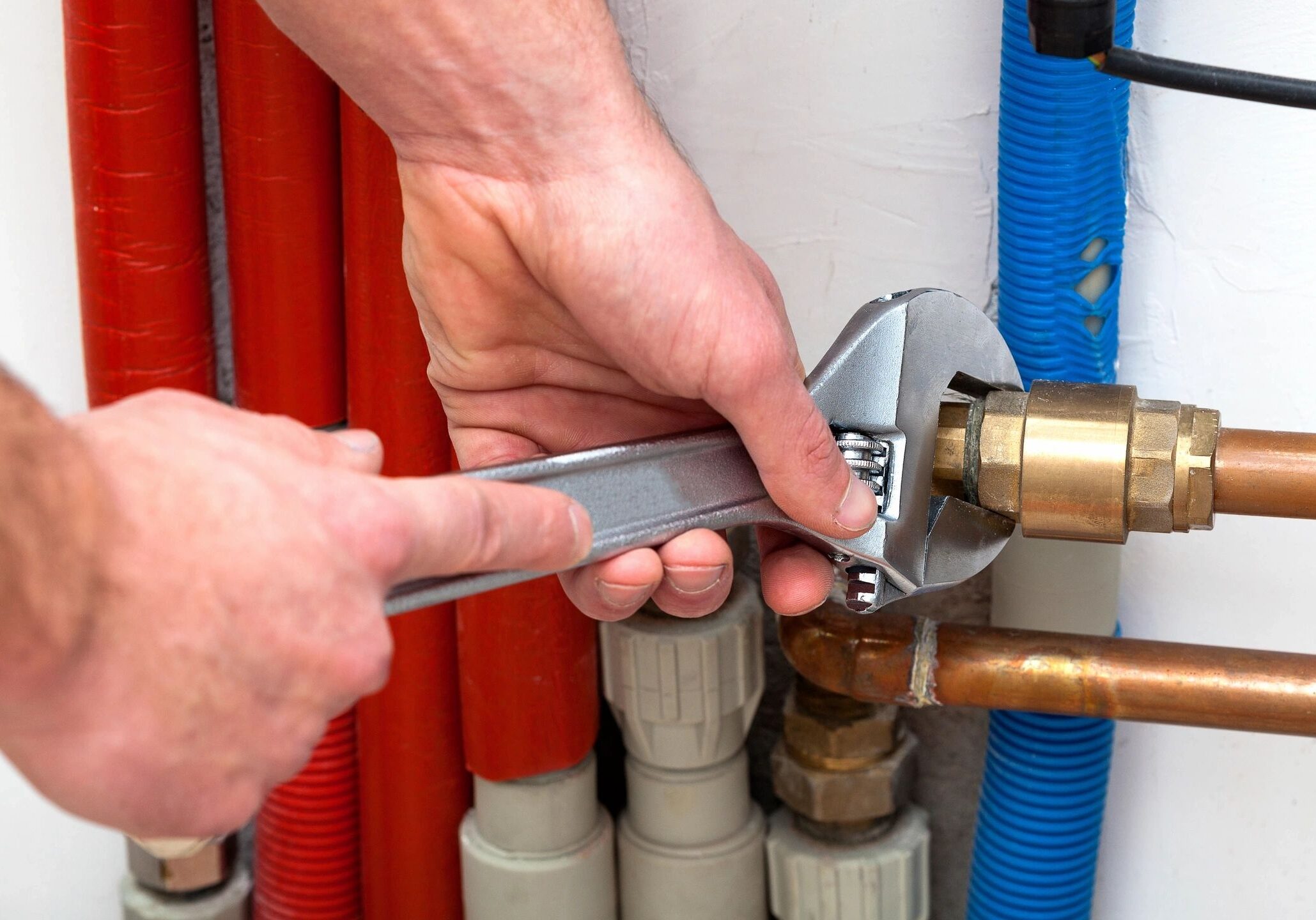 Hands using a wrench to tighten a pipe fitting.