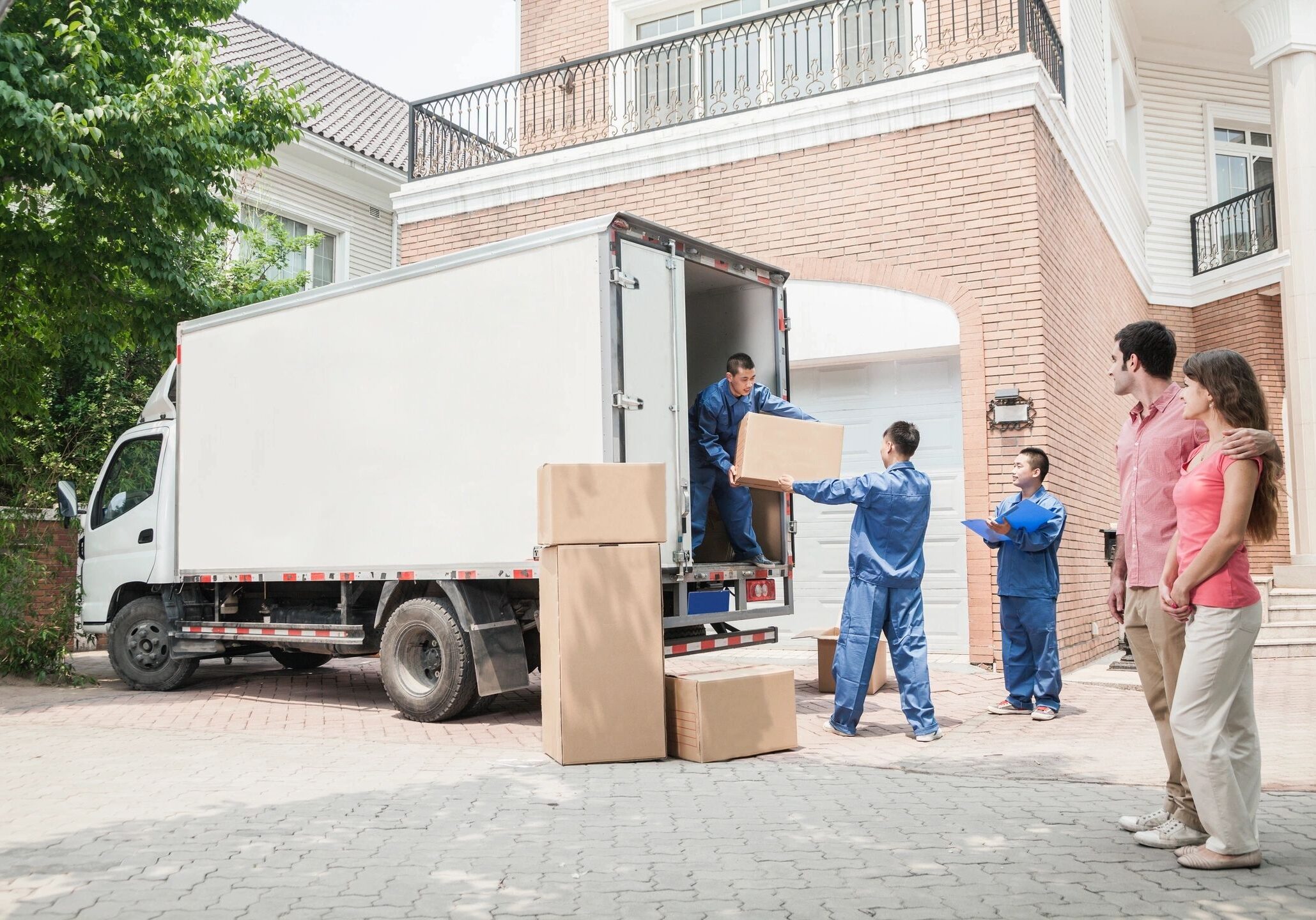 Workers unloading boxes from a large truck outside a brick building.