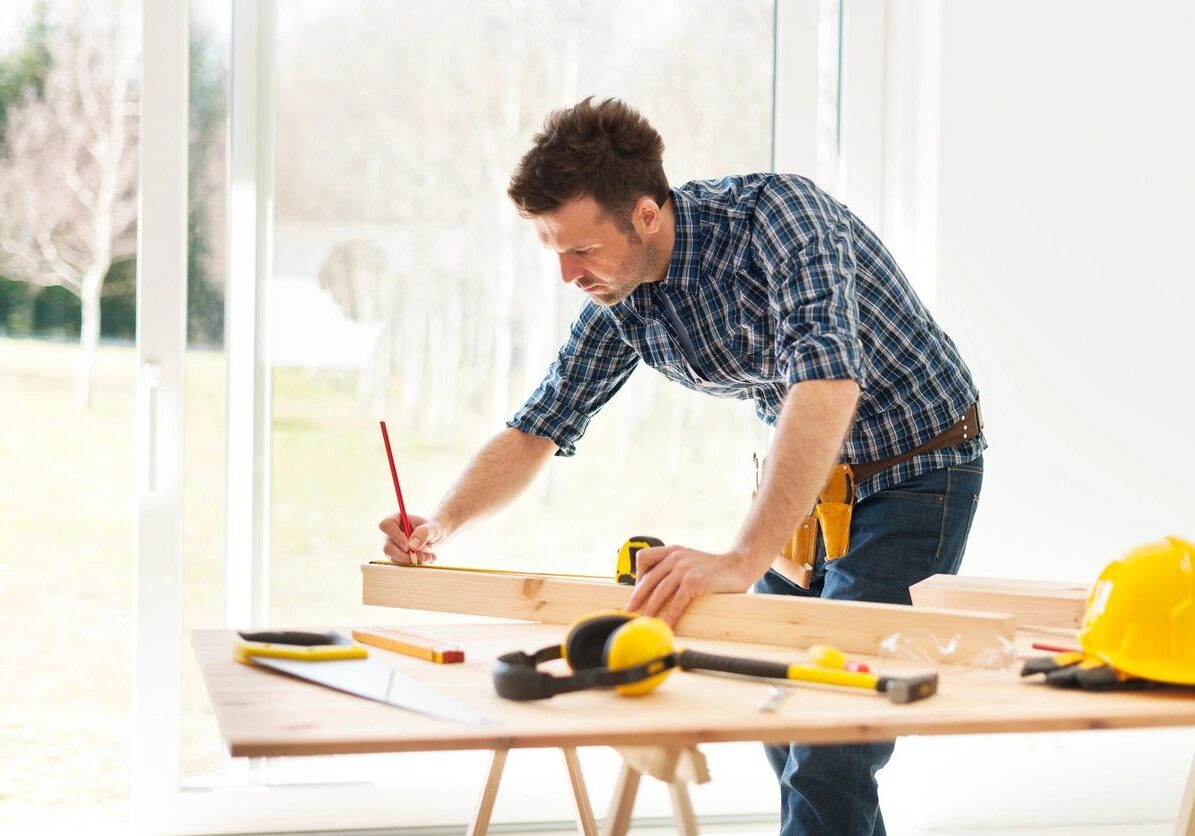 A man measuring wood with a tape measure on a workbench.