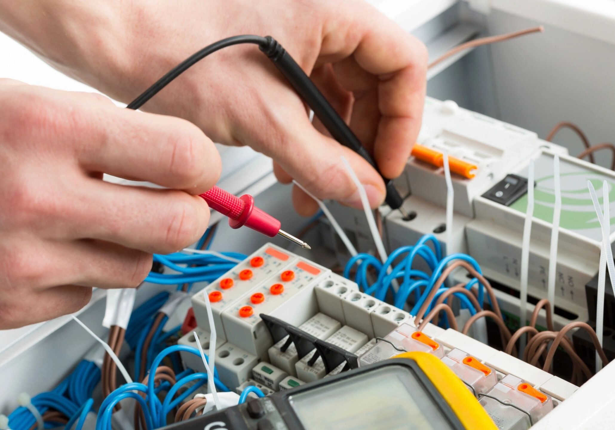 Electrician testing wiring connections with tools inside a control panel.