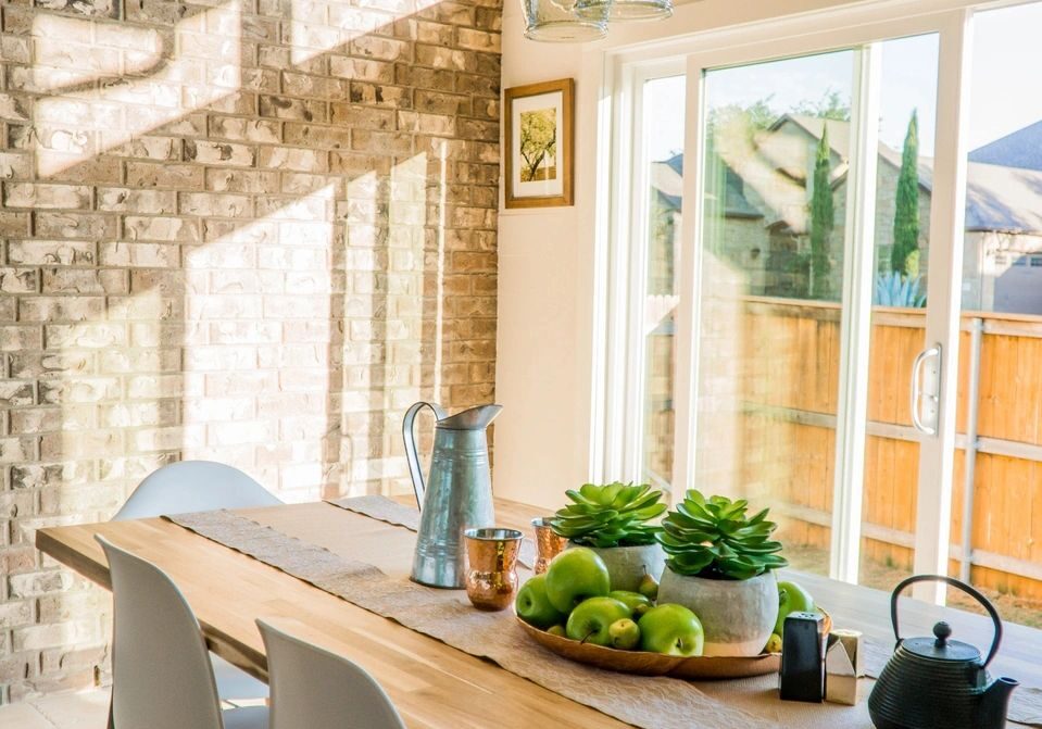 Bright dining area with wooden table and white chairs by large windows.