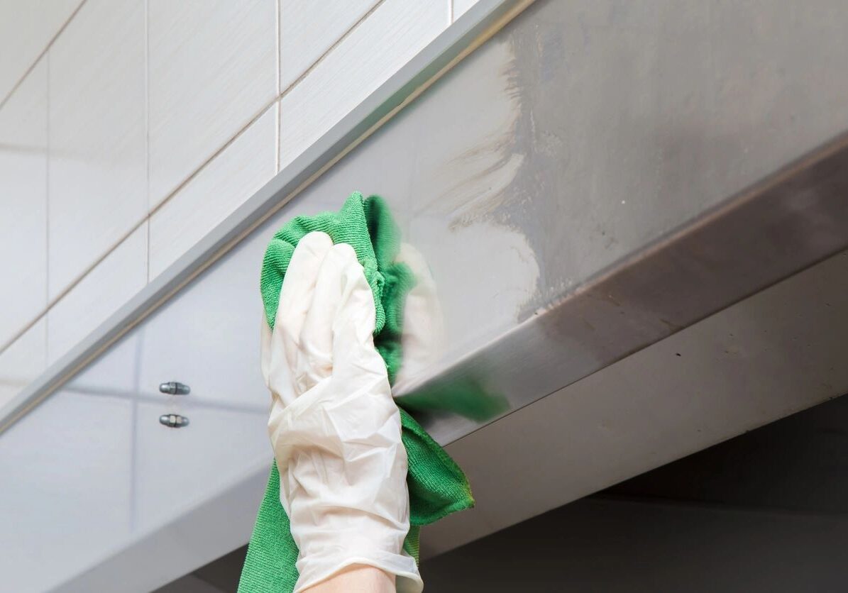 A gloved hand cleaning a stainless steel surface with a green cloth.