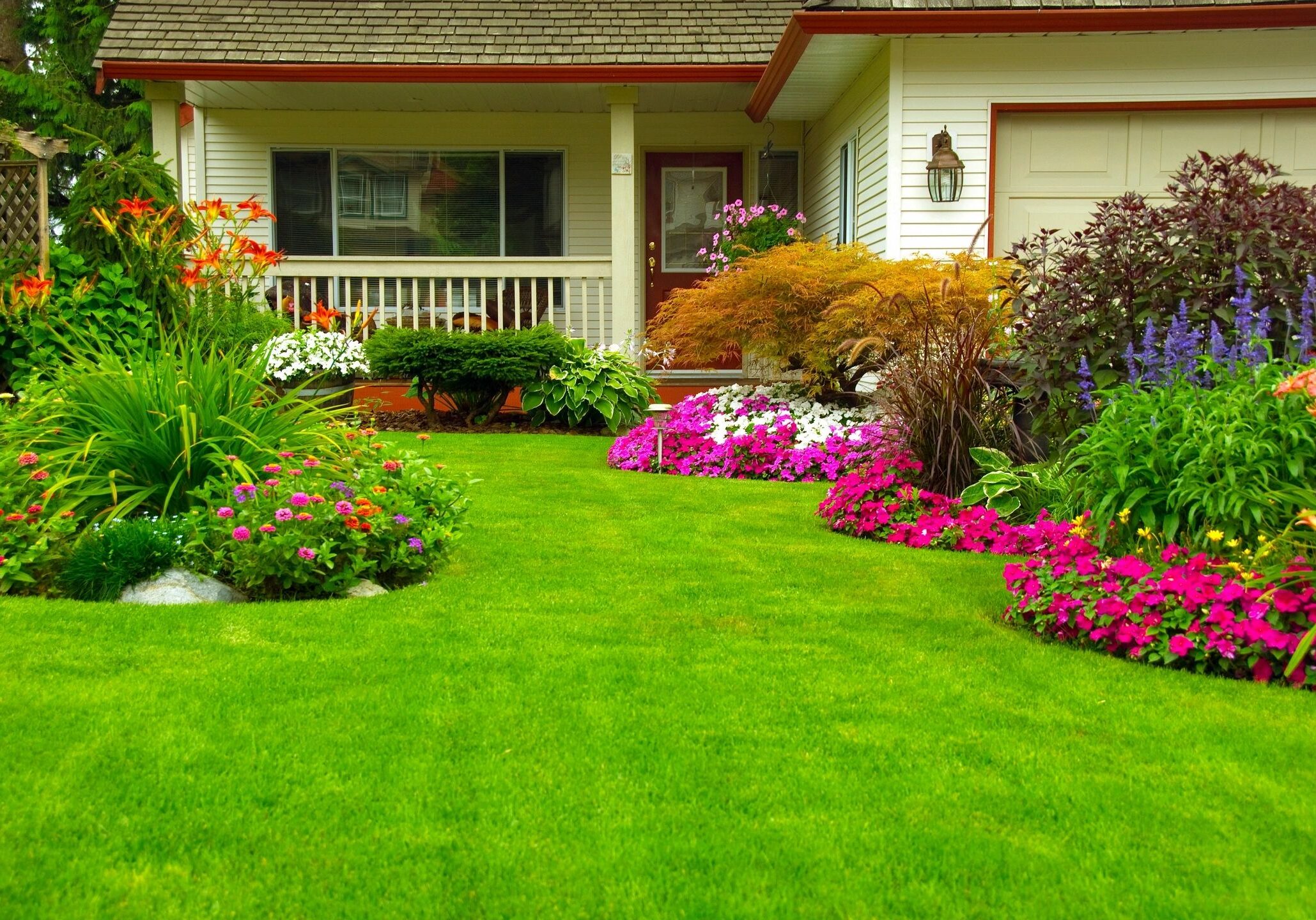 Vibrant garden with lush green lawn and colorful flowers in front of a cozy house.