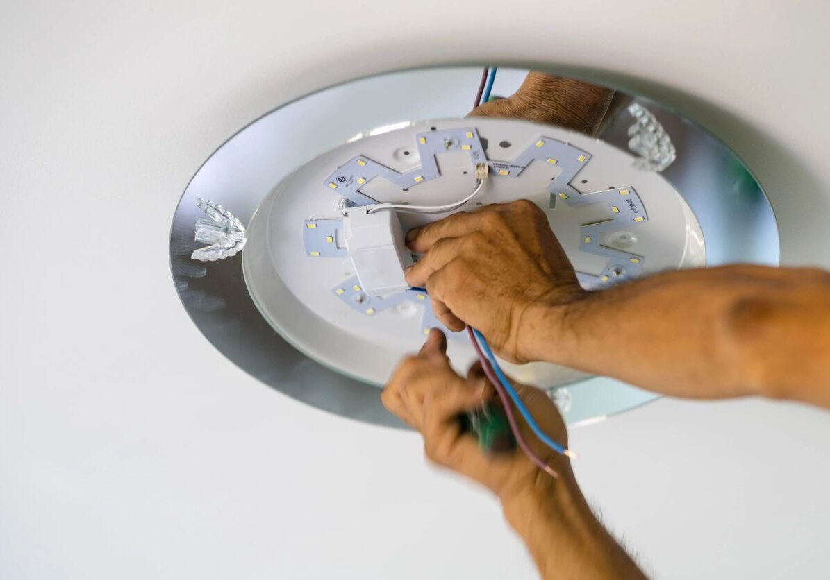 Hands installing a ceiling light fixture with tools.
