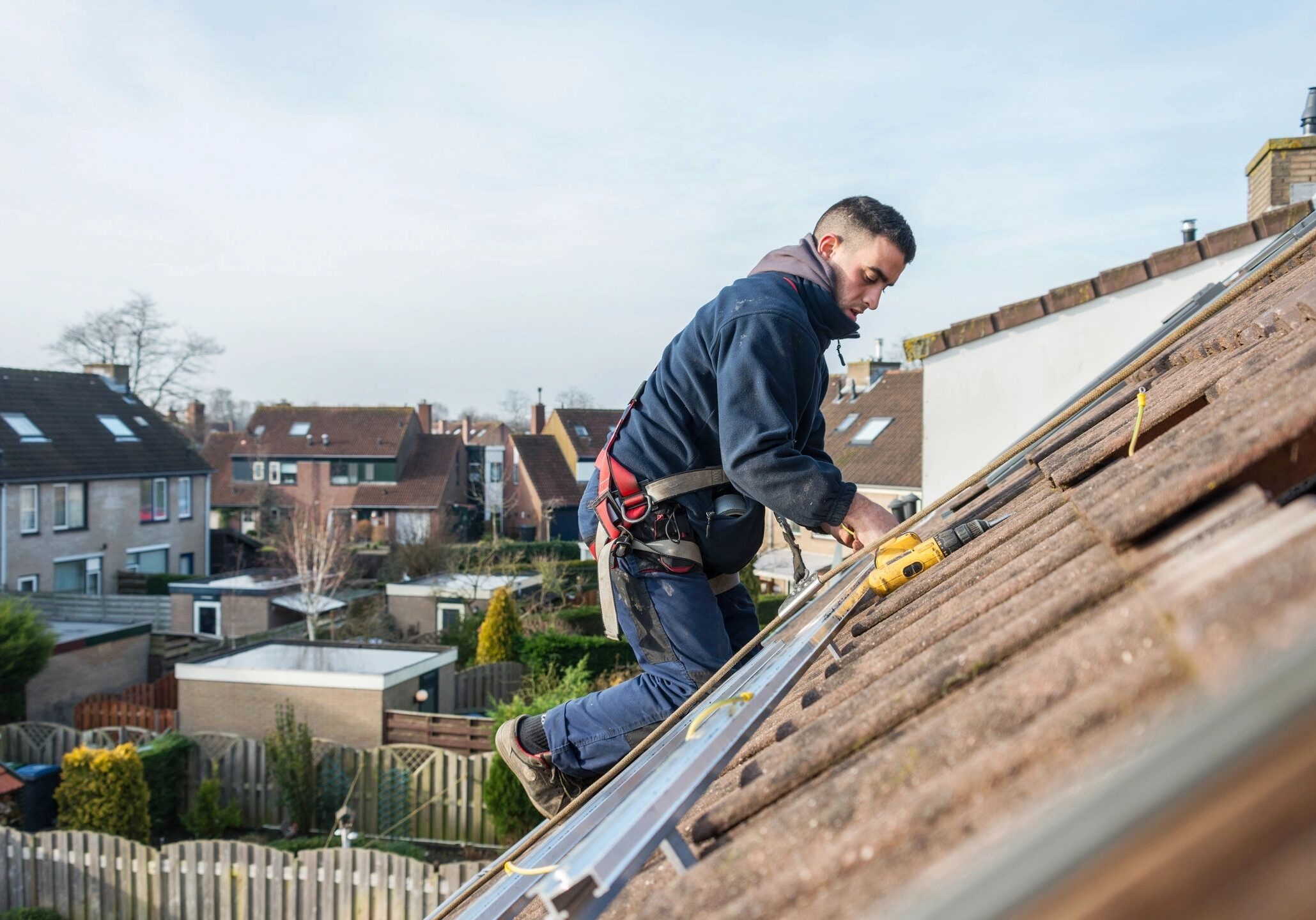 A worker installs solar panels on a rooftop under a clear sky.