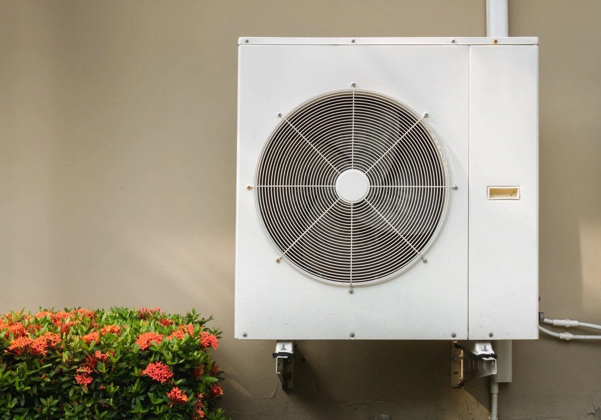 Outdoor air conditioning unit mounted on a wall near plants.