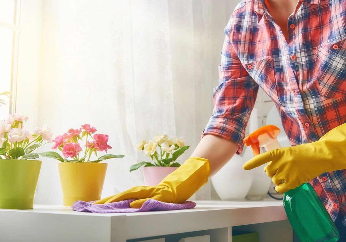 Person cleaning a white table wearing yellow gloves and a red plaid shirt.