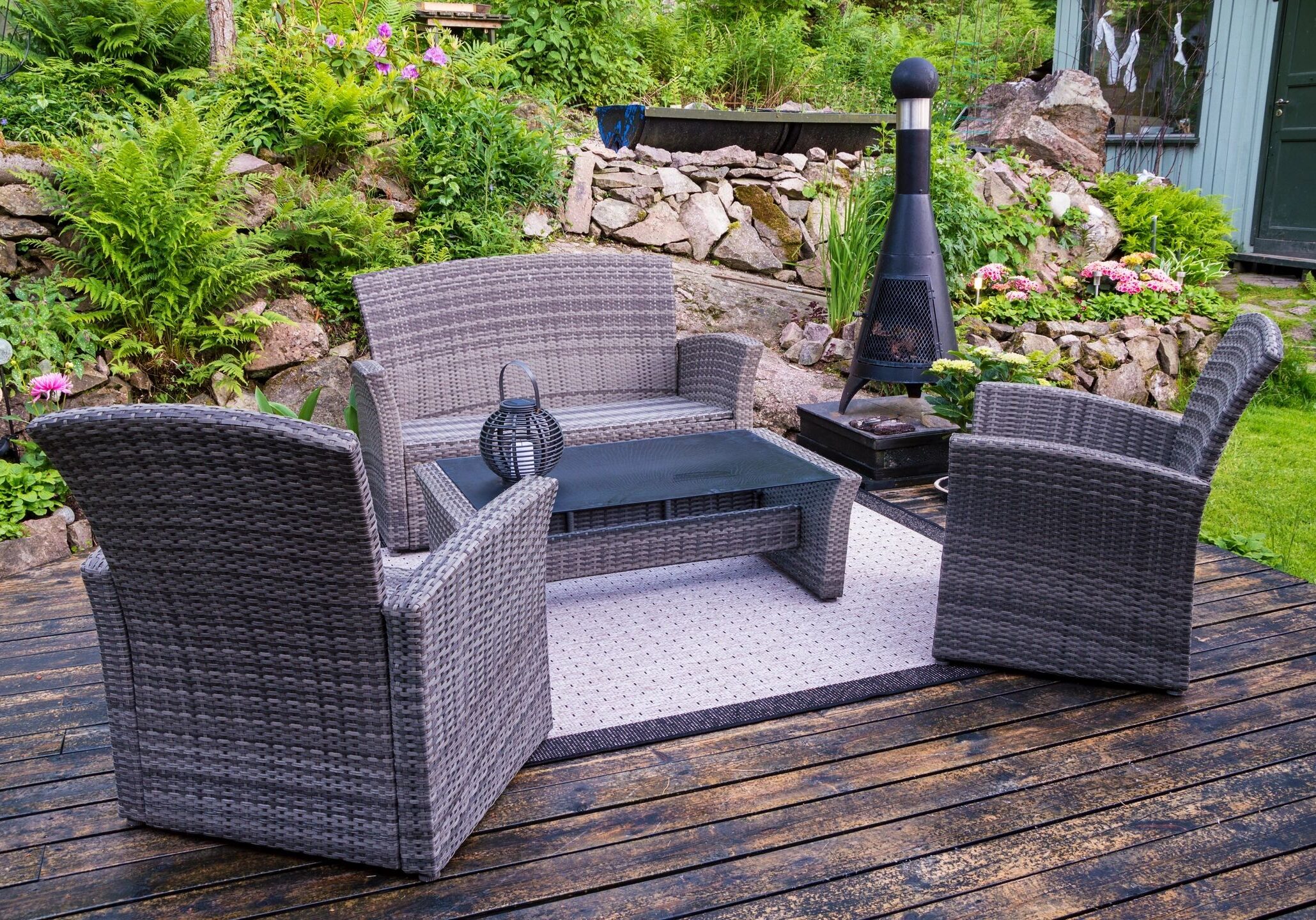 Outdoor wicker patio set with loveseat, chairs, and glass-top table on wooden deck.